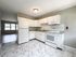 renovated kitchen, stone countertops, overhead light, white cabinets, refrigerator, range with hood, tile backsplash, tile floor, view into living room with big windows