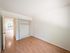 Bright, spacious bedroom with wood flooring and open closet, leading to a sunlit living area with garden view.