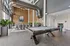 Shared co-working space with large desks, comfortable seating, a pool table, potted plants, and floor to ceiling windows.