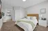 A bedroom featuring plush carpeting and warm overhead lighting. The room includes a comfortable bed, stylish furnishings, and large windows allowing natural light to fill the space.