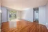 Spacious living room featuring elegant hardwood floors, large windows, and a view of lush greenery.