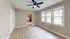 Sunlit room with hardwood flooring, ceiling fan, and large windows leading to a modern kitchen.