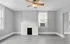 Bright living room with modern gray walls, wooden flooring, a ceiling fan, and white brick fireplace.