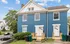 Front view of a charming blue duplex with white accents and small porches on a sunny day.