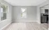 Open, sunlit living area with light wood flooring and adjacent modern kitchen.