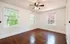 Spacious room with polished hardwood floors, featuring three large windows and a ceiling fan.