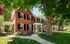 Lovely colonial-style brick house with black shutters and a lush green lawn under a mature tree.