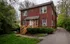 Classic two-story red brick house with lush greenery and inviting wooden steps.