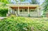 Charming bungalow with a spacious front porch nestled in lush greenery, offering serene living amidst nature.