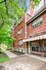 Charming red brick apartment building with large windows, surrounded by lush greenery on a serene sidewalk pathway.