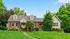 Charming brick home with a vibrant green door, nestled in lush greenery and surrounded by mature trees, perfect for tranquil living.