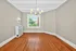 Bright and inviting room with elegant hardwood floors, a large window offering lush green views, and a modern chandelier adding chic style.
