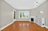 Elegant living room with gleaming hardwood floors, a classic white fireplace, large bright windows, and a modern light fixture.