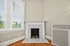 Charming living space with elegant white marble fireplace and large sunlit windows featuring blinds.