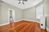 Bright and inviting bedroom with elegant hardwood floors, large window, and modern ceiling fan, leading to a chic en-suite bathroom.