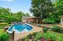 Charming backyard oasis featuring a sparkling swimming pool, inviting wooden deck, and lush garden, surrounded by serene greenery.
