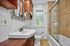 Charming bathroom featuring elegant wood cabinetry, a stylish decorative mirror, and a sleek glass-enclosed bathtub with stone tiles.