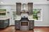 Elegant kitchen with modern stainless steel oven, dark wood cabinets, and chic tile backsplash, illuminated by large windows overlooking lush greenery.