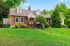 Charming brick house with gabled roof set in lush greenery, featuring a welcoming front porch and vibrant landscaping.