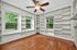 Charming room with built-in shelves, hardwood floors, and large windows overlooking lush greenery, featuring a ceiling fan for comfort.