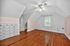 Charming attic bedroom with white walls, warm hardwood floors, built-in storage, and a ceiling fan.