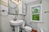 Bright and inviting bathroom featuring modern fixtures, a chic white vanity, and a window with a lush green view.