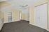 Bright room with built-in shelves, a ceiling fan, beige walls, and plush carpeting, ideal for a versatile living space.