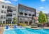 Modern apartment complex featuring a stylish facade with balconies, surrounding a vibrant outdoor pool area with lounge chairs, under a clear blue sky.
