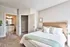 Bright and cozy bedroom with elegant beige headboard, plush white bedding, and access to a modern ensuite bathroom.