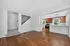Bright and inviting open-plan space featuring a modern kitchen with stainless steel appliances and elegant wood cabinetry, seamlessly connected to a cozy living area with warm hardwood flooring and adjacent carpeted staircase.