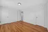 Bright bedroom with elegant hardwood flooring and pristine white walls, featuring two closed doors and one open door revealing a glimpse of the hallway.