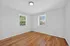 Bright, inviting room with polished hardwood floors and two sunlit windows overlooking lush greenery.
