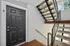 Modern apartment entrance featuring a sleek black door, stylish staircase, and bright natural lighting.