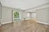 Bright and airy living room with sleek wood flooring, large windows, and sliding glass doors leading to a private balcony with green views.
