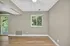 Bright, empty room with modern hardwood floors, neutral walls, and a ceiling fan, featuring a window view of lush greenery and direct access to a cozy balcony.