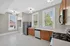 Bright and modern kitchen with stainless steel appliances, wooden cabinetry, and elegant tile flooring. Large windows provide ample natural light, creating an inviting cooking space.