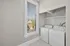 Bright laundry room with modern appliances, ample shelving, and a large window offering natural light in a contemporary apartment.