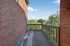 Charming urban balcony with rustic brick walls and wooden railing, offering a serene view of lush greenery and the cityscape.