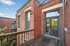 Charming outdoor deck with rustic wooden railing on a brick building, offering a serene view and abundant natural light through large glass doors.