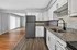 Modern kitchen with granite countertops, sleek white cabinets, and stainless steel appliances adjacent to an open living area with wood flooring.