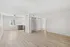 Bright, spacious living area with sleek wooden flooring and modern open-plan kitchen featuring pristine white cabinets.