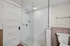 Modern bathroom showcasing a sleek glass shower with white subway tiles and hexagonal floor tiles, alongside a classic white door and toilet. Clermont Condominiums apartments in East Walnut Hills.