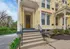 Charming yellow brick townhouse with elegant porch entry, framed by decorative columns and lush greenery.