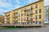 Charming yellow brick apartment building with classic fire escapes and a welcoming wooden deck, set against a vibrant blue sky.