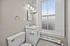 Bright, modern bathroom featuring a classic white vanity with marble countertop, elegant lighting, and large window providing natural light.