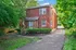 Charming red brick house with lush greenery and a private driveway, offering cozy suburban living.