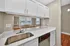 Modern kitchen with sleek white cabinetry, elegant marble countertops, stainless steel sink, and view into a bright, sunlit living area with hardwood floors.
