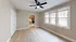 Open living room with wood flooring, a ceiling fan, and large windows leading to a kitchen area.