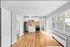 Bright and modern kitchen with sleek white cabinetry, stainless steel appliances, and warm hardwood floors, featuring large windows for natural light.