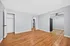 Bright and spacious room featuring elegant hardwood floors and a modern ceiling fan, leading to an adjacent area with sleek kitchen flooring.